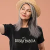 Elegancka kobieta w dojrzałym wieku w czarnej koszulce z napisem Boska Babcia i słomkowym kapeluszu