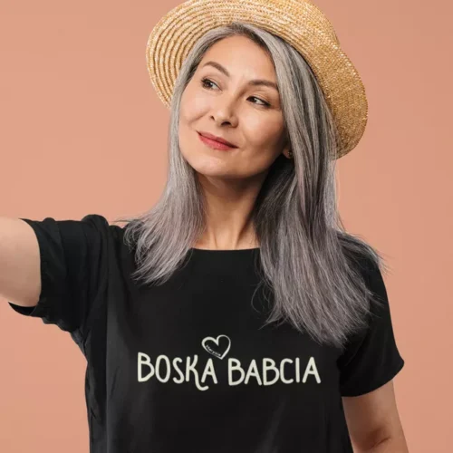 Elegancka kobieta w dojrzałym wieku w czarnej koszulce z napisem Boska Babcia i słomkowym kapeluszu