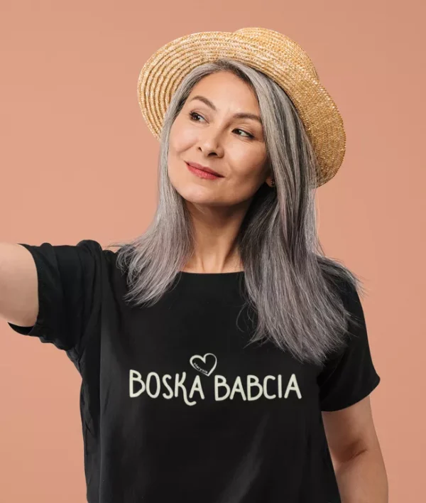 Elegancka kobieta w dojrzałym wieku w czarnej koszulce z napisem Boska Babcia i słomkowym kapeluszu