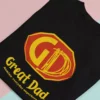 Czarna koszulka z nadrukiem Great Dad i personalizacją złożona na dwukolorowym tle