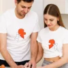 Szczęśliwa para w białych, personalizowanych koszulkach z nadrukiem połówki serca, stojąca w kuchni. Idealne koszulki dla par na rocznicę lub Walentynki.