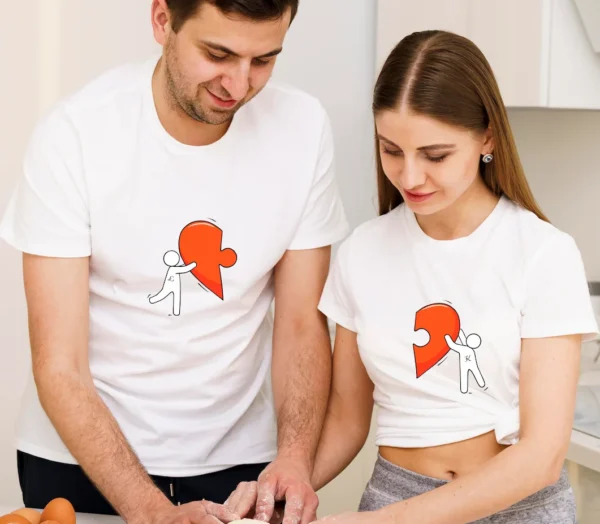 Szczęśliwa para w białych, personalizowanych koszulkach z nadrukiem połówki serca, stojąca w kuchni. Idealne koszulki dla par na rocznicę lub Walentynki.