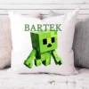 Personalizowana poduszka z zieloną, pikselową postacią w stylu Minecraft i imieniem "Bartek" na białym tle, ułożona na łóżku w otoczeniu szarych i puszystych poduszek.