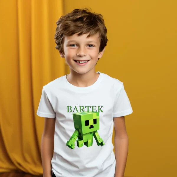 Chłopiec w białej koszulce z nadrukiem zielonej, pikselowej postaci i imieniem "Bartek" na tle żółtej zasłony, uśmiechnięty i radosny.