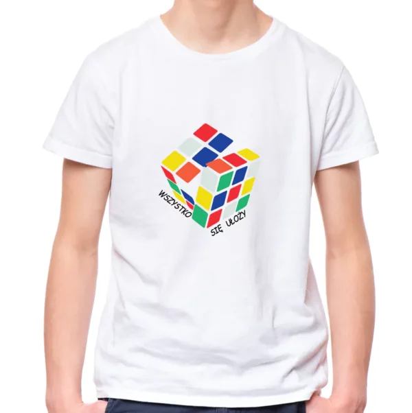 Biała koszulka dziecięca unisex z kolorowym nadrukiem przedstawiającym rozkładającą się Kostkę Rubika i czarnym napisem "WSZYSTKO SIĘ UŁOŻY" wokół niej. Model prezentuje koszulkę na jasnym tle.