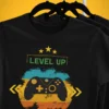 Czarna koszulka dla gracza Level Up! z kontrolerem i napisem „Unlocked Level 19”, wisząca na wieszaku.