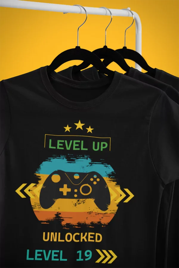 Czarna koszulka dla gracza Level Up! z kontrolerem i napisem „Unlocked Level 19”, wisząca na wieszaku.