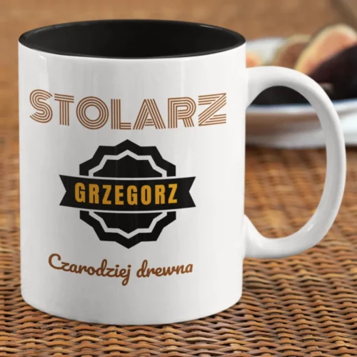 Personalizowany kubek z czarnym wnętrzem, napisem 'STOLARZ GRZEGORZ Czarodziej drewna' i figami w tle, na rattanowej podkładce.
