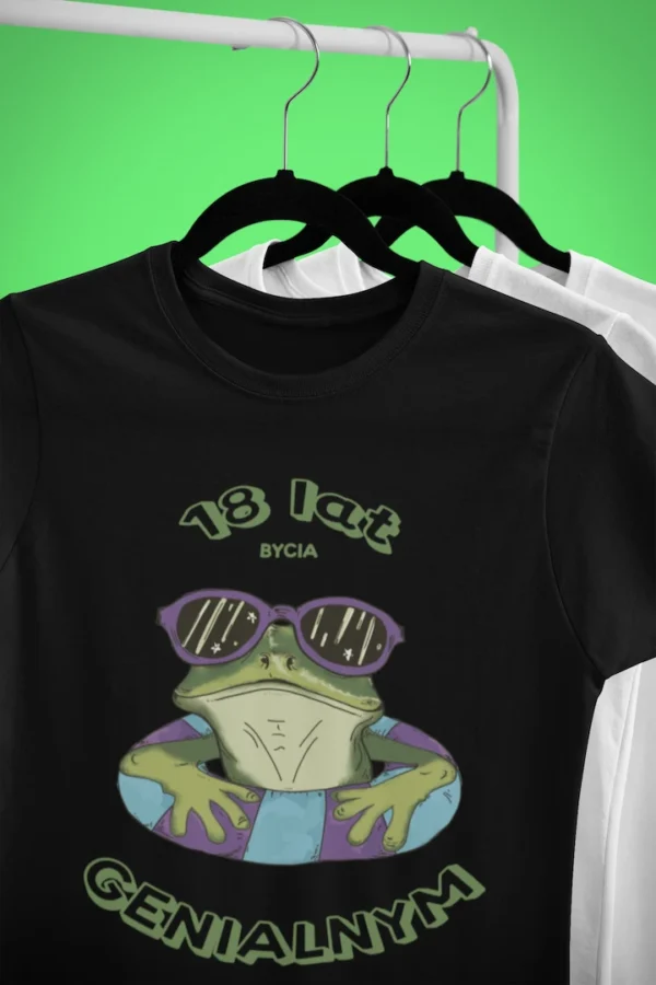 Czarna męska koszulka urodzinowa z zabawnym nadrukiem żaby w okularach i personalizowanym wiekiem 'X lat bycia GENIALNYM', wisząca na wieszaku, widok z przodu.