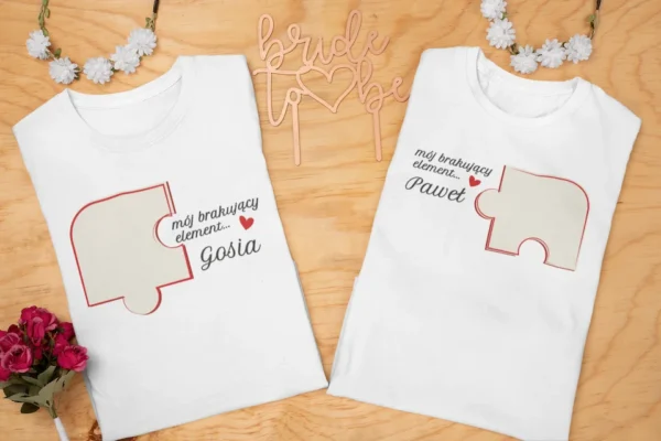 Dwie białe koszulki z nadrukiem puzzla i imionami Gosia oraz Paweł na drewnianym tle