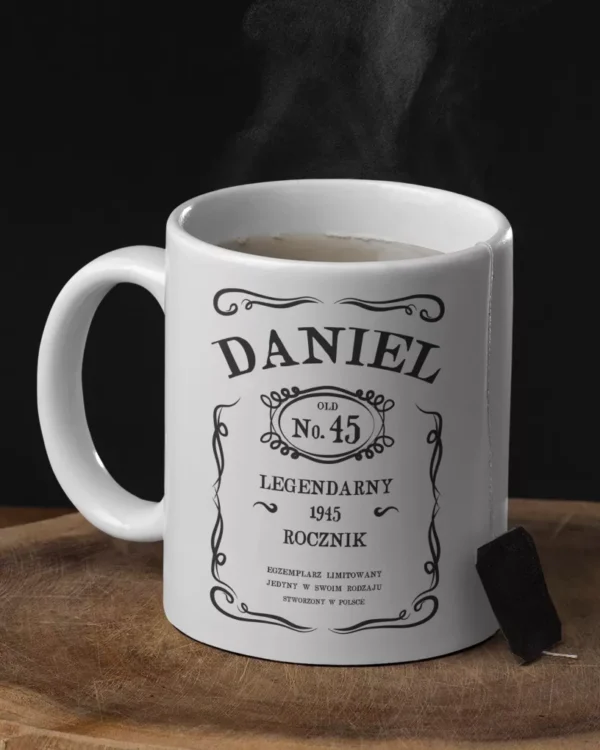 Biały kubek z napisem Daniel Legendarny Rocznik 1945 na drewnianym podkładzie z parującym napojem