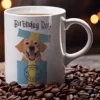Biały ceramiczny kubek z napisem Birthday Boy i grafiką psa wyskakującego z prezentu na tle ziaren kawy