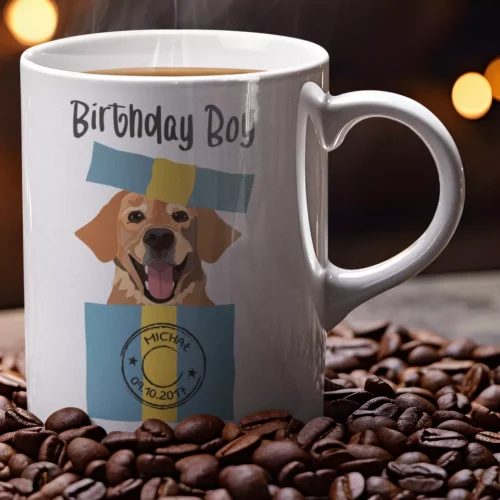 Biały ceramiczny kubek z napisem Birthday Boy i grafiką psa wyskakującego z prezentu na tle ziaren kawy
