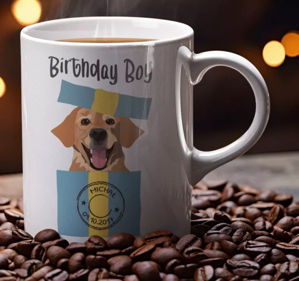 Biały ceramiczny kubek z napisem Birthday Boy i grafiką psa wyskakującego z prezentu na tle ziaren kawy