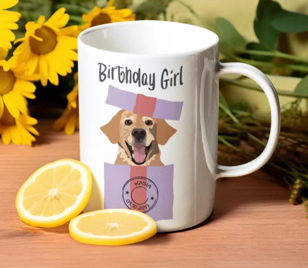 Biały ceramiczny kubek z napisem Birthday Girl i grafiką psa w prezencie, stojący na drewnianym stole obok cytryn i słoneczników.