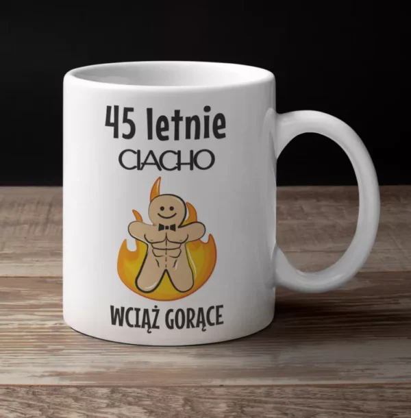 Biały ceramiczny kubek z napisem 45 letnie ciacho wciąż gorące i grafiką umięśnionego piernika w ogniu